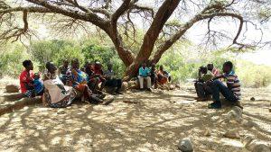Picture of various Ugandans sitting under a tree for an interview 