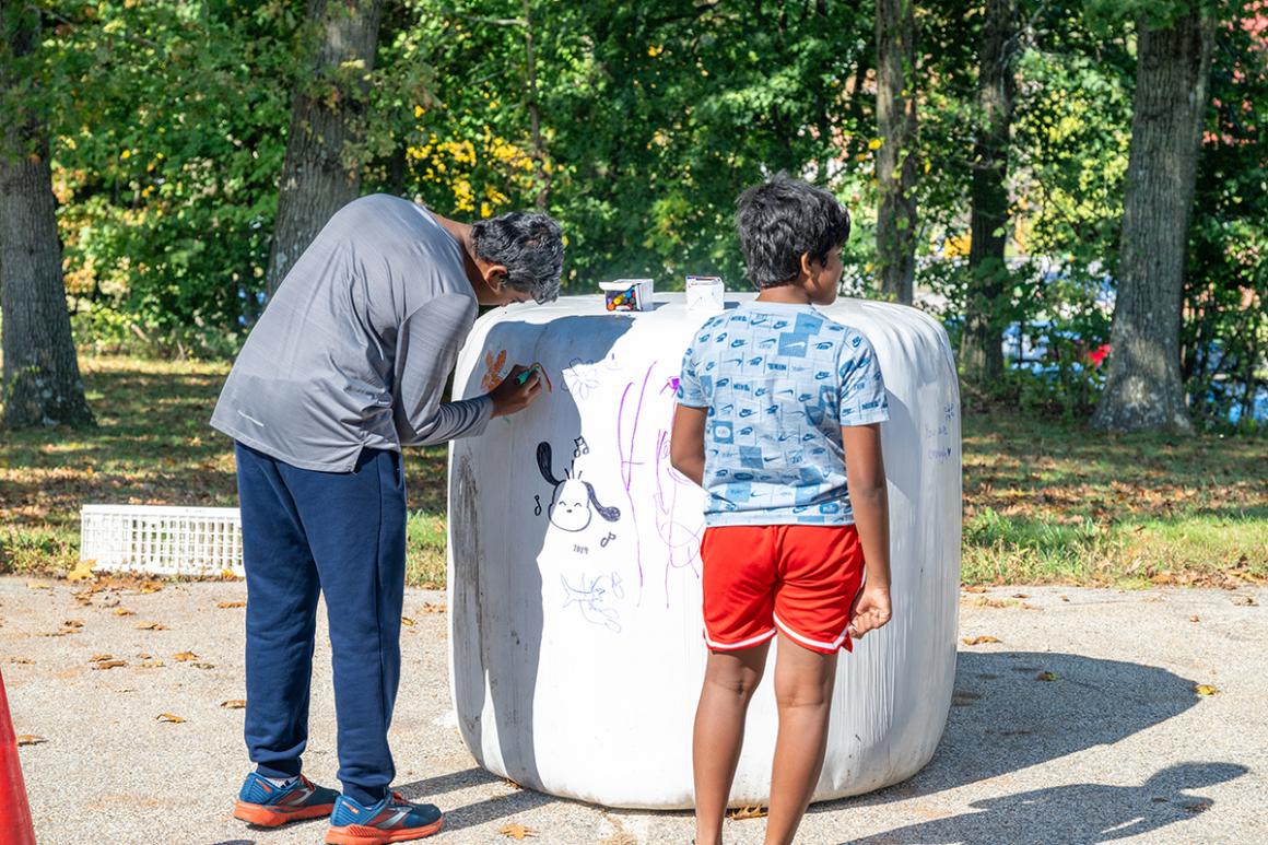 An adult and child draw with markers outside on a white plastic covered hay bale.