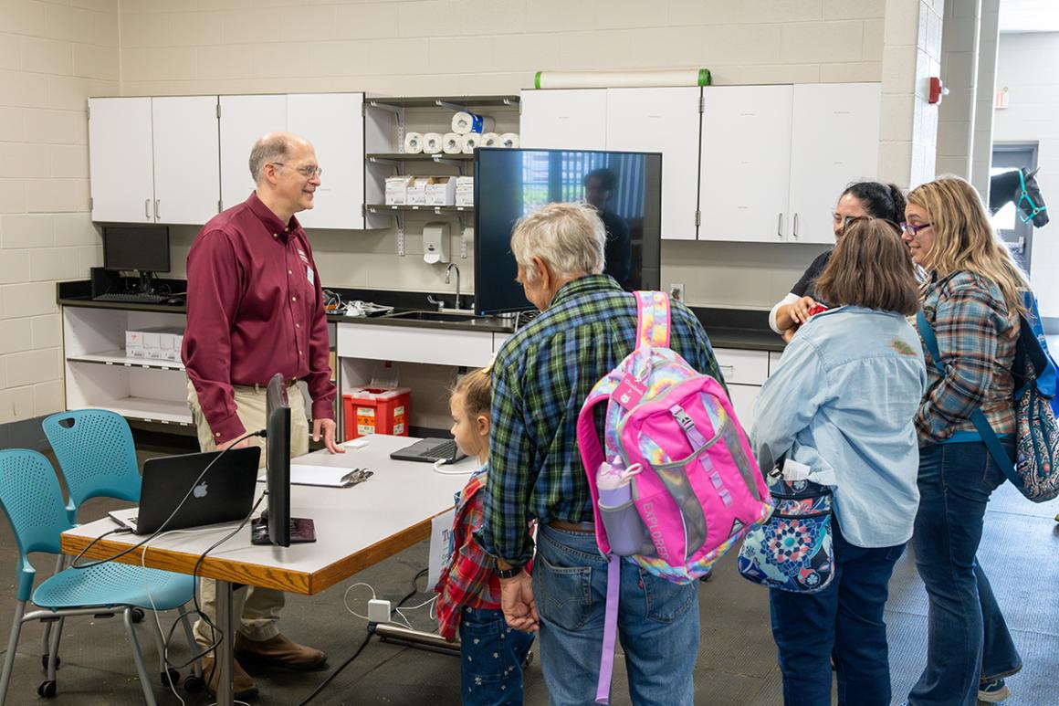 Smiling faculty member talks to individuals at a table