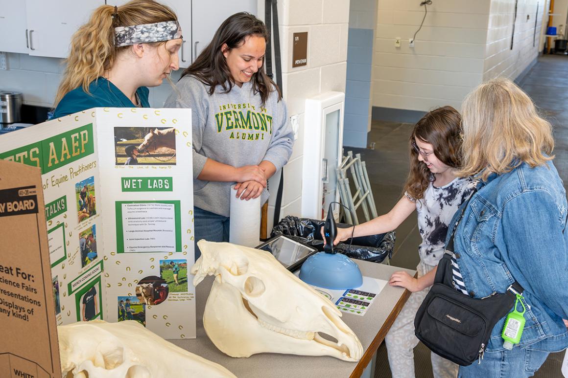 Two individuals show a child how to hold an ultrasound probe at a demonstration table.