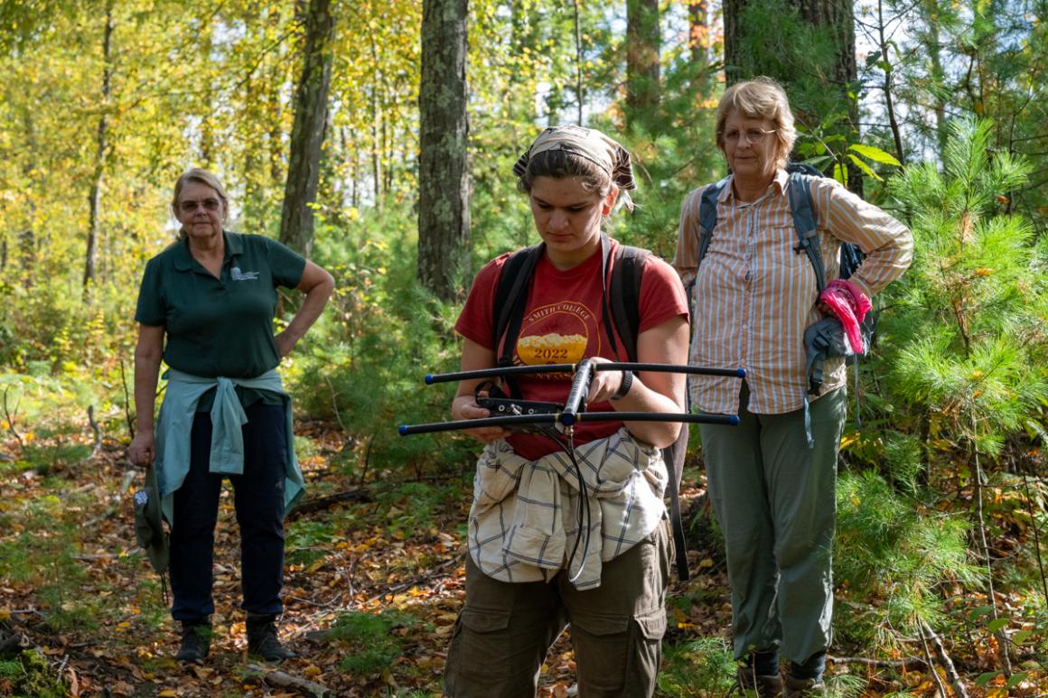 Three individuals outside in the woods with one holding onto a black transmitter device.