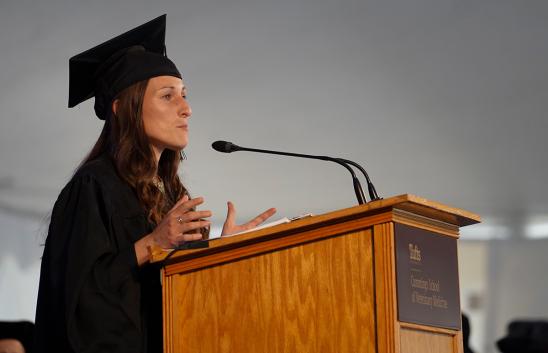 Graduate student wearing black cap and gown speaking at a podium