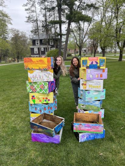 Two females accompany stacks of a dozen colorfully-painted bee boxes.