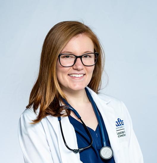 A woman with light brown hair wearing glasses and a white lab coat.