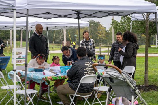 A group of individuals of all ages working at a table doing an activity outdoors.