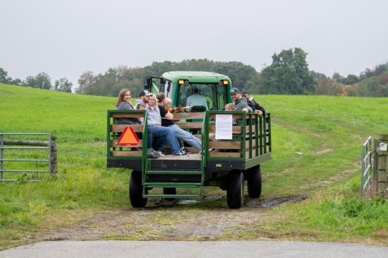 Individuals riding on a tractor through a field of grass.