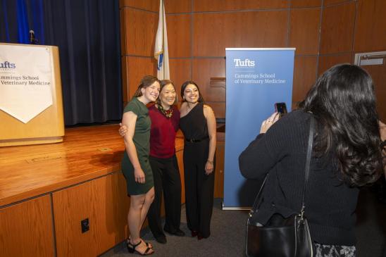 three people standing close together posing for a photo in front of a stage.