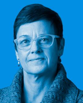 Dr. Carrie Wood wearing eye glasses, a collared sweater and has short dark hair. Image has a blue filtered background.