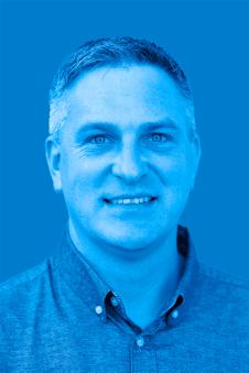 Adam Ward smiling and wearing a collared shirt. Image has a blue filter.