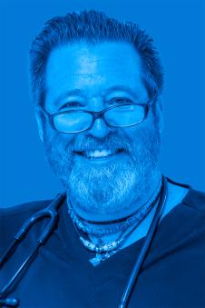 Gregory Wolfus smiling wearing glasses with short hair and a beard and moustache. Image has a blue filter.