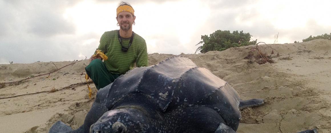 A man kneeling next to a huge tortoise