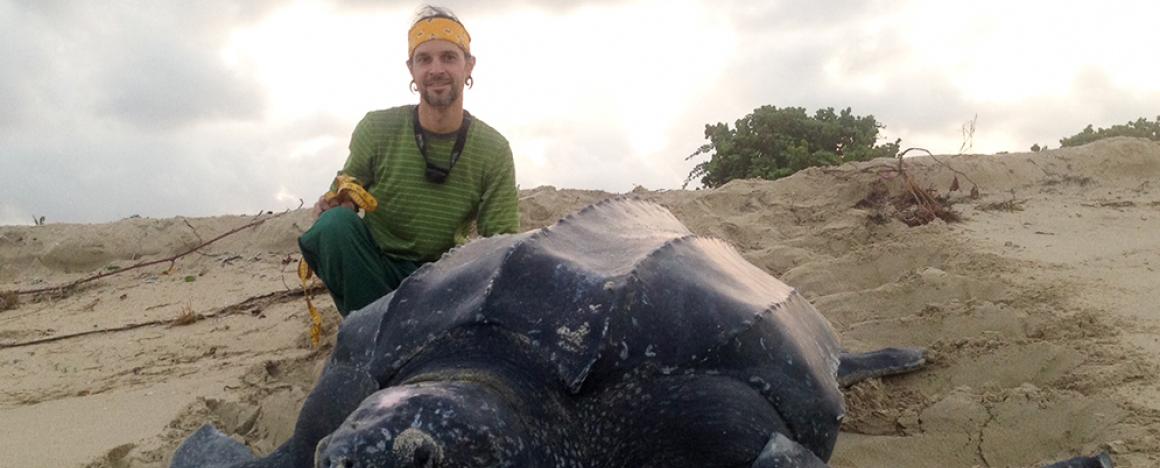 A man kneeling next to a huge tortoise 