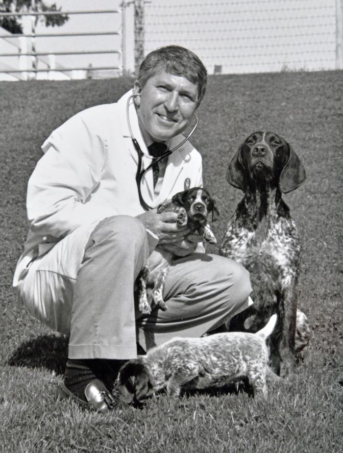 Jim Ross kneeling with two puppies and their mother