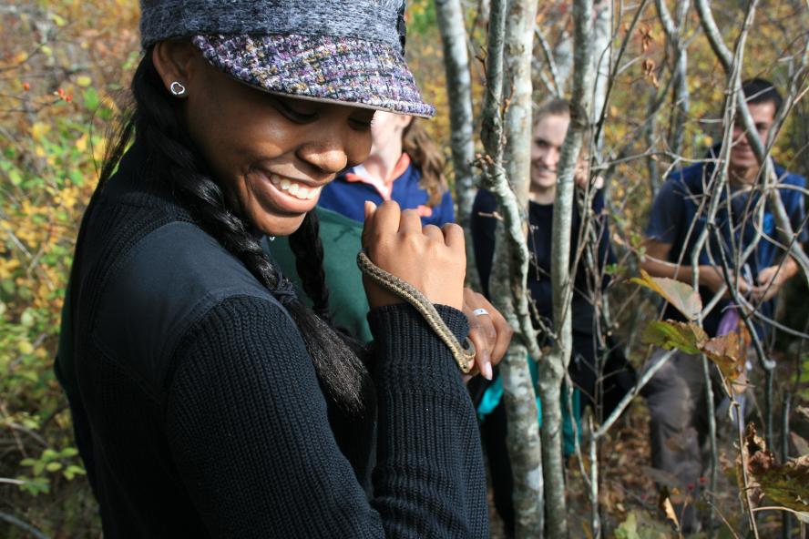 black woman wearing cap, smiling and holding a garter snake