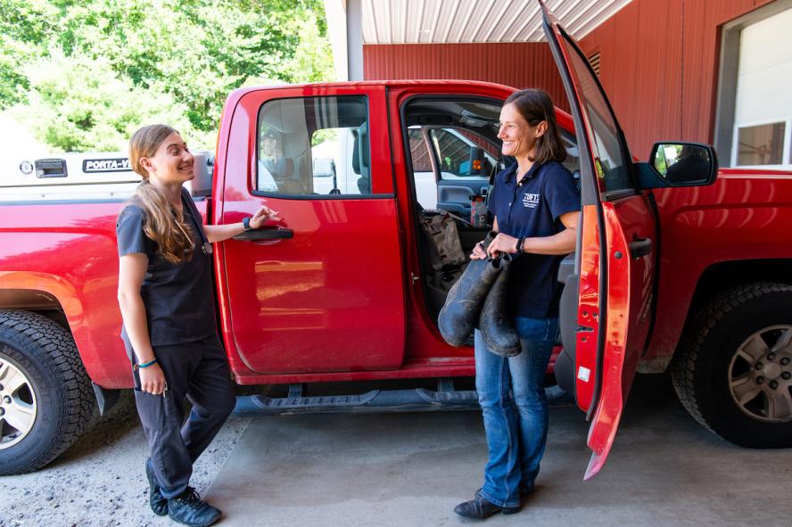 Two female field veterinarians standing against a red truck talking.