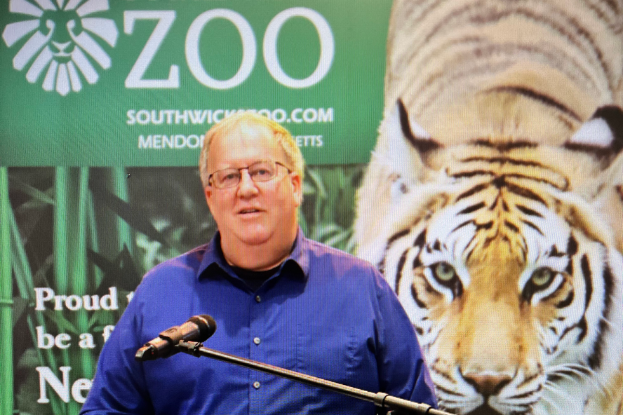 Peter Brewer standing at podium with a Southwick Zoo banner behind him.