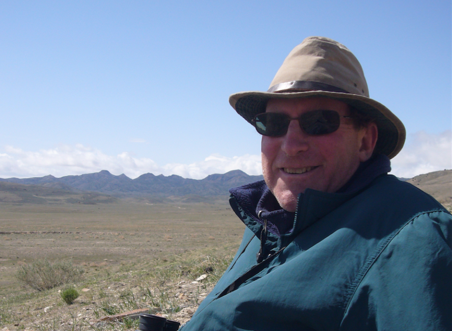 Man in glasses and hat on a plateau with grass and mountains. 