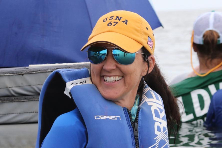 woman smiling, in the water, wearing a yellow baseball cap, sunglasses and a blue life vest 