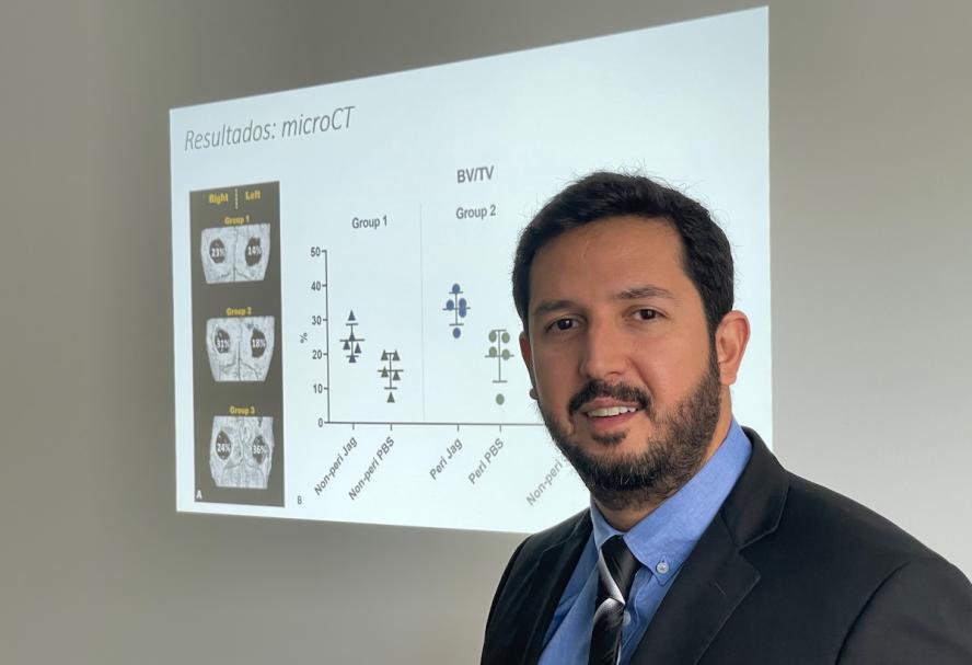 Man with dark hair and beard and wearing a suit presenting on bone research and using a smart board on wall