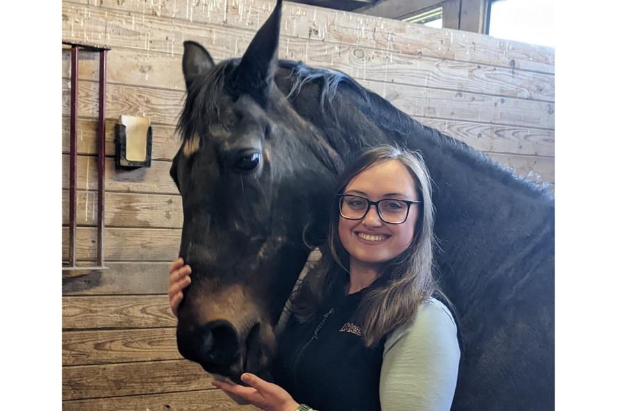 a young lady wearing glasses standing with her horse holding his snout