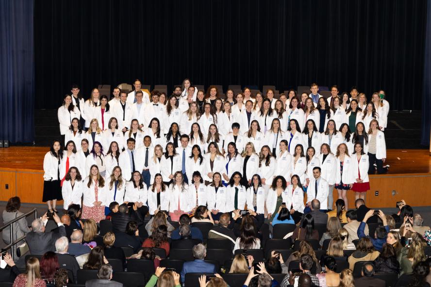 Ninety-five veterinary students wearing white coats standing on a stage