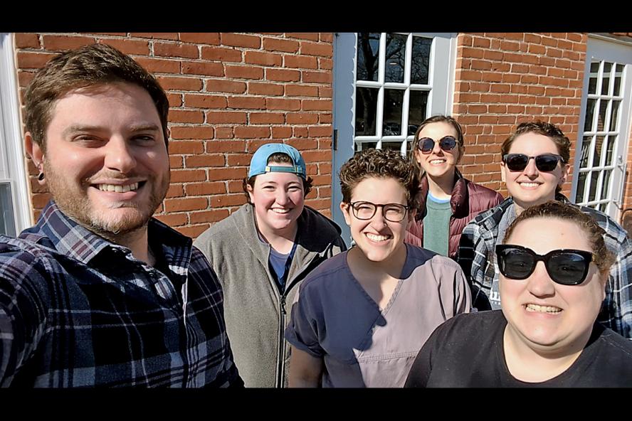 Group of diverse people standing in front of a brick building smiling while taking a group selfie