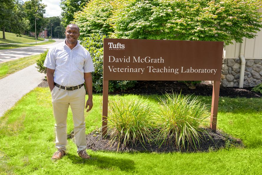 an individual wearing a white shirt and khaki pants stands outside by a sign reading “David McGrath Veterinary Teaching Laboratory”