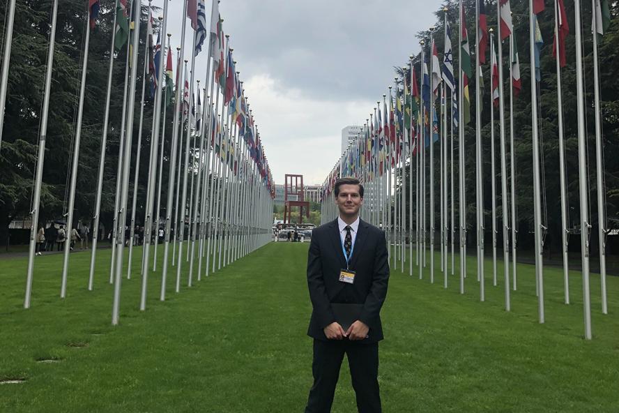 A young man standing in the middle of a row of tall international flag posts