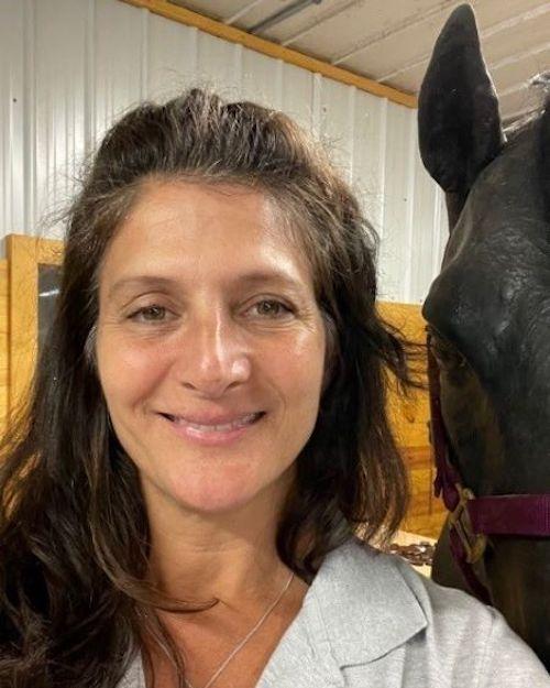 A smiling woman with long brown hair standing next to a black horse.