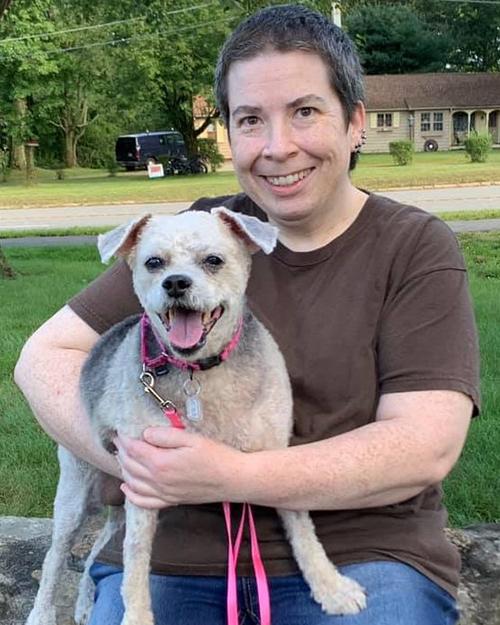 A smiling person with short hair holding her dog on her lap.