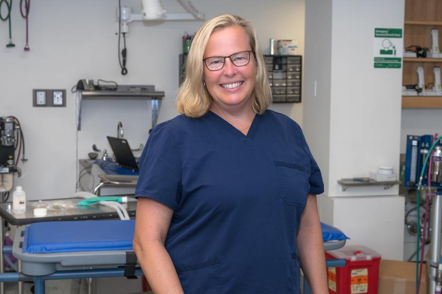 A smiling woman with blond hair wearing glasses and navy blue hospital scrubs