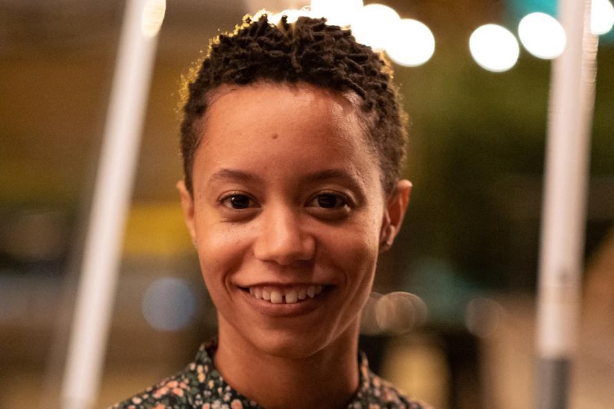 A smiling person presenting as a female with short curly hair and dark skin