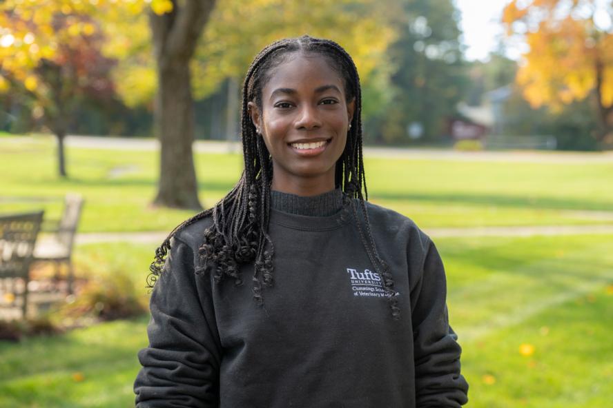 A smiling dark skinned individual with long, dark hair wearing a dark sweatshirt.