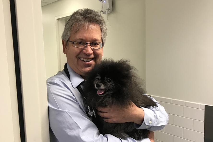 a smiling person wearing glasses and holding a little black fluffy dog