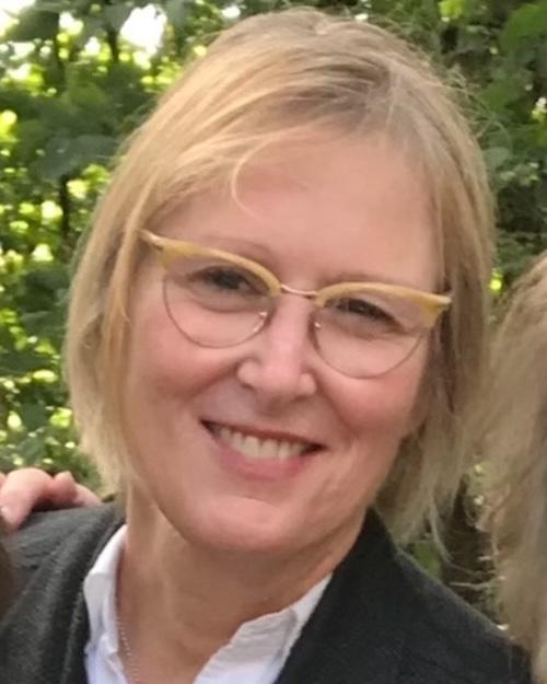 a smiling individual with short blond hair wearing glasses.