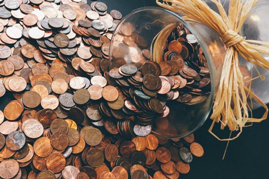 a pile of coins being emptied from a glass jar onto a table