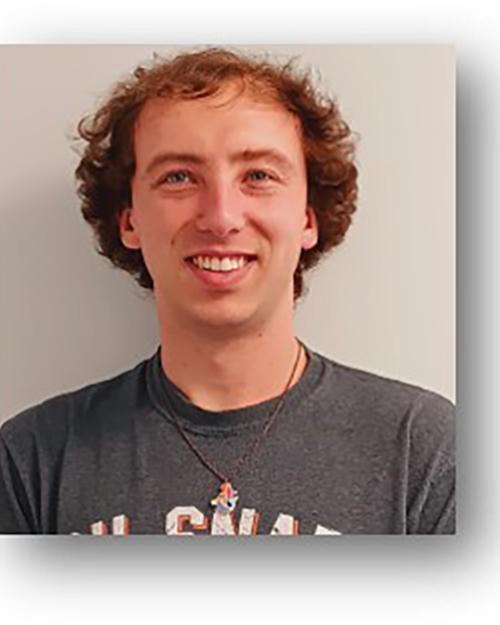 a smiling individual with short wavy hair wearing a grey tshirt.