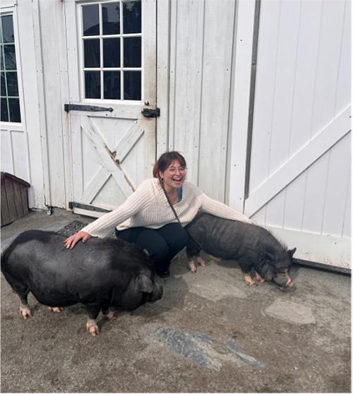 a smiling individual kneeling in between two pet pigs