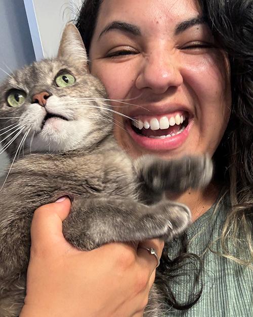 an individual laughing while holding a grey and white cat.