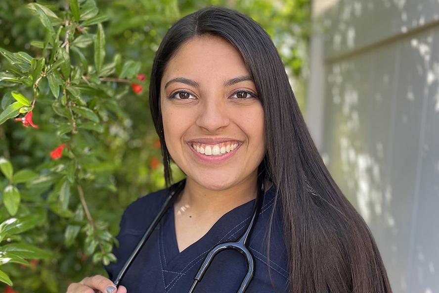 Person smiling with long dark hair and a dark V-neck shirt standing outdoors.