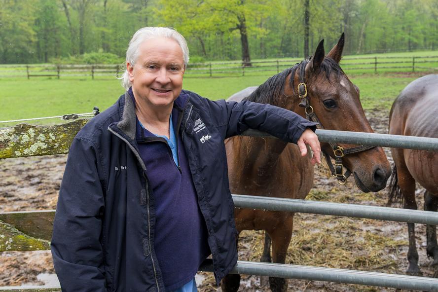 Professor Emeritus Carl Kirker-Head leaning against a railing with horses in the background.