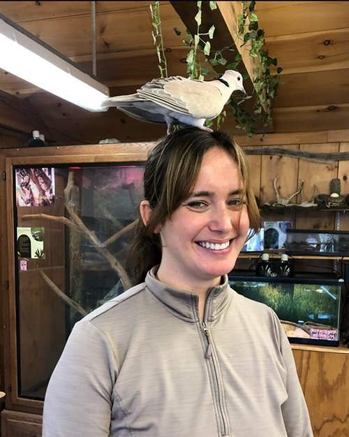 Sofia Fernandes smiling with a bird standing on top of her head.