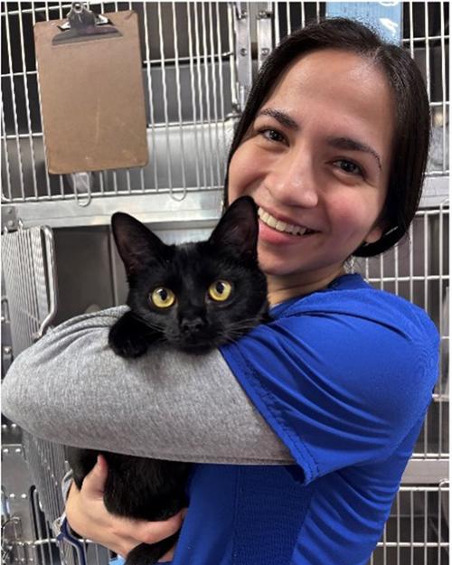 Mariana Pavia smiling and holding a black cat in a veterinary hospital ward.