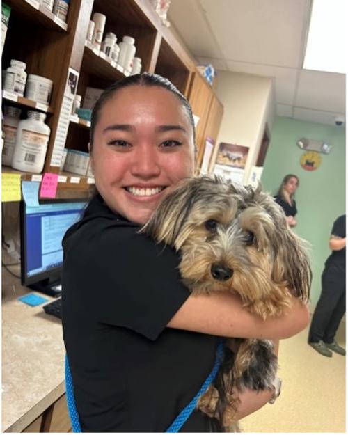 Nonni Schwartz smiling and holding a small dog in a veterinary medical facility.