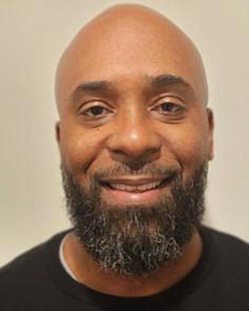 Ralph Eugene, MSN, APRN, PMHNP-BC, Psychiatric Nurse Prationer. He has a beard and mustache, is smiling and wearing a black shirt.