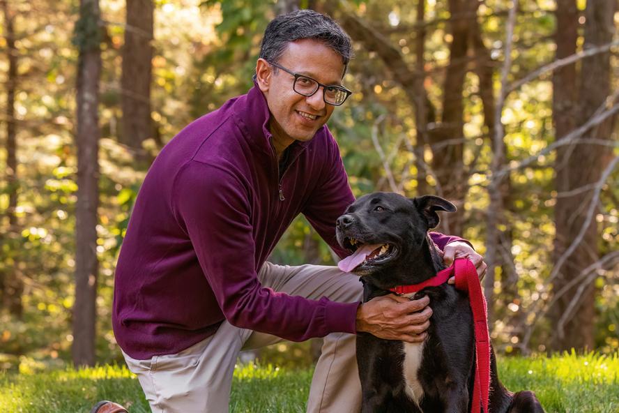 A person with black glasses outside with a black dog wearing a red leash.