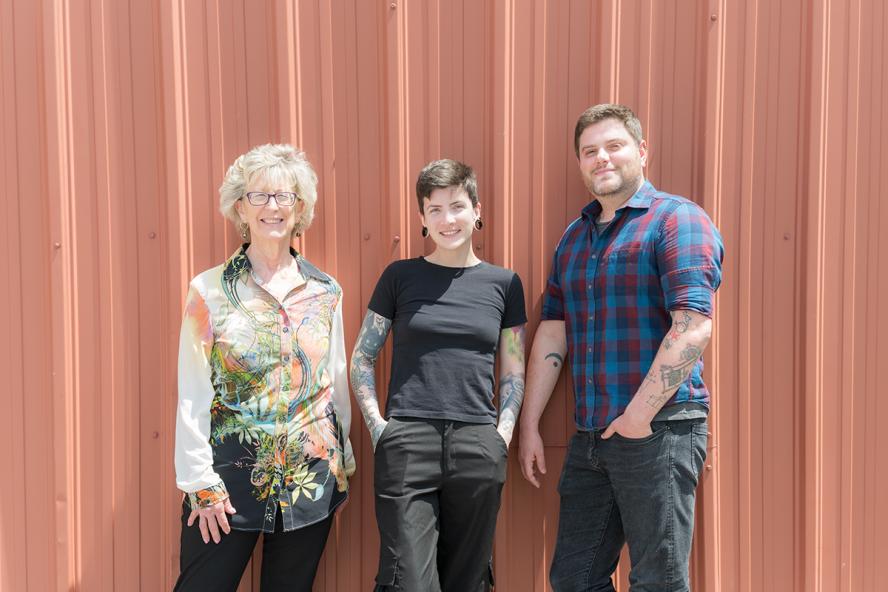 Two female and one male clinician, casually dressed, smile while standing in front of a red wall.