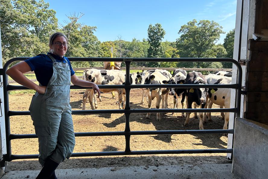 Dr. Isabelle Louge standing against a barn gate. There are black and white cows on the other side of the gate grazing.
