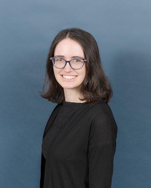Abigail Kaplan has shoulder length dark brown hair, is smiling, wearing glasses and a black shirt and black blazer.
