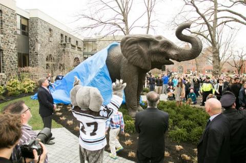 A tarp half covers a big elephant statue, with people surrounding it.